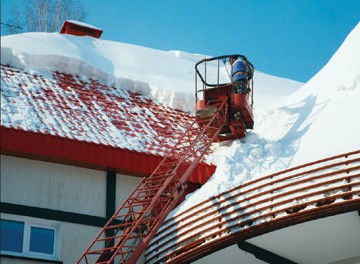 snow being removed from a roof with a man lift