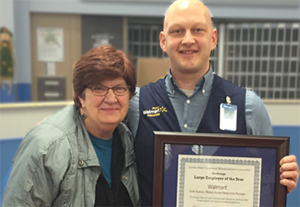 A man and a women pose together. The man holds a framed certificate. 